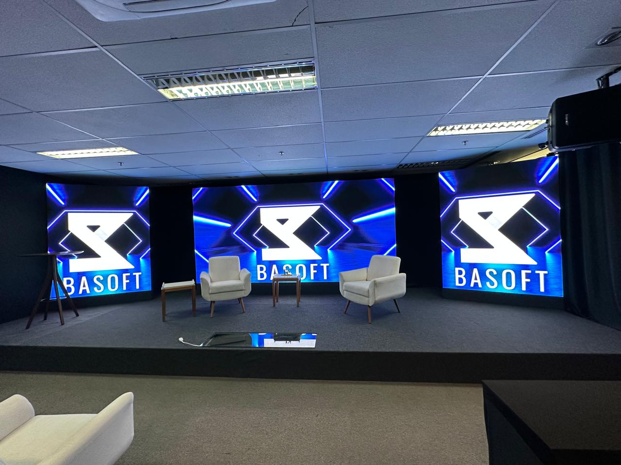 Palco do auditório da BASOFT com poltronas e painéis de LED, pronto para o formato talks