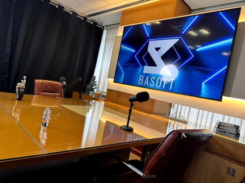 Estúdio de podcast da BASOFT com a mesa de madeira, microfones e a tela de LED ao fundo